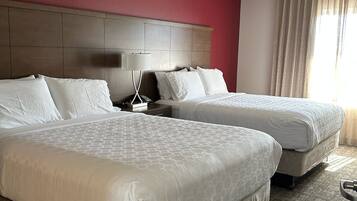 Habitación de hotel con dos camas, una pared de acento roja, una lámpara de techo y un ventanal con cortinas.