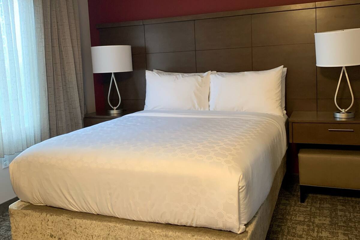 Ein Hotelzimmer mit einem großen Bett, zwei Nachttischen inklusive Lampen, einer Kopfteil und einem Teppichboden.
