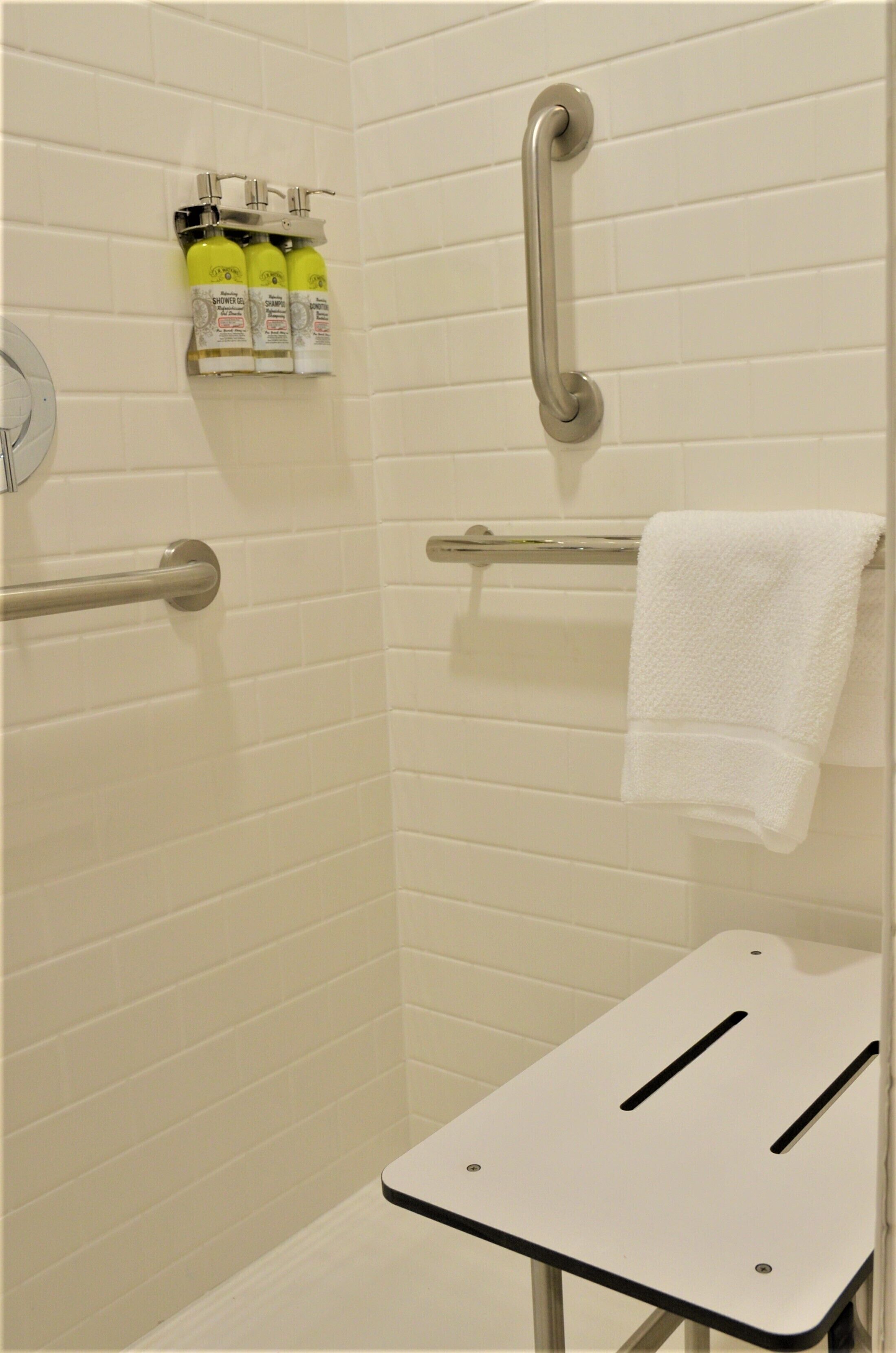 A shower area with grab bars, a towel rack, and toiletries.