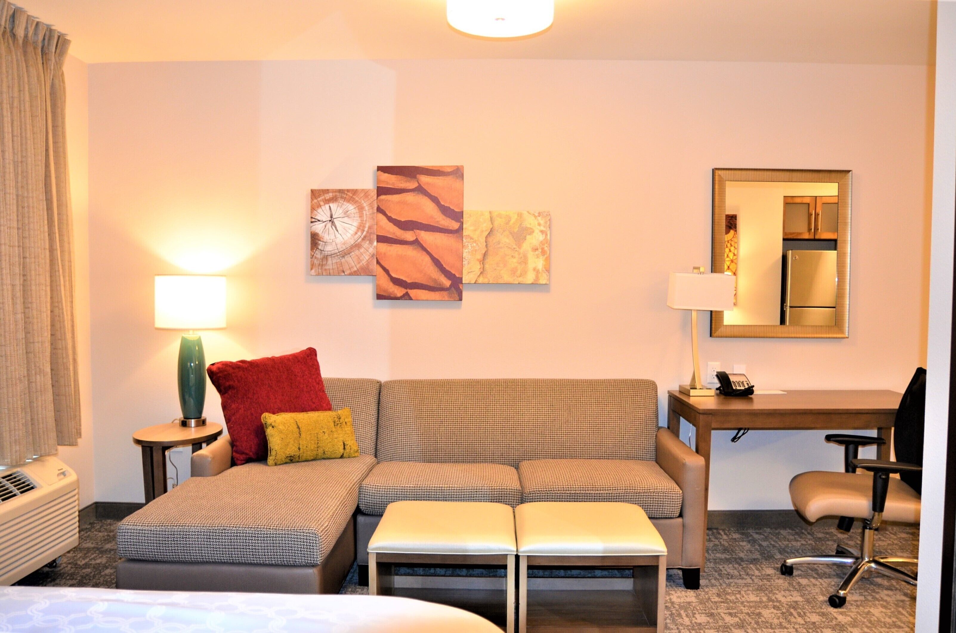 A hotel room with a sofa, a desk, a chair, a lamp, and artwork on the wall.