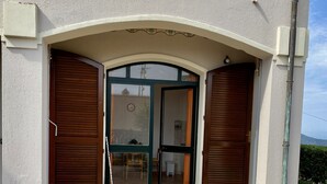 En bygningseingang med en brostensbelagt indkørsel, en grønrammet glasdør og træpersienner.