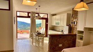 A compact kitchen with white cabinets, a stone accent wall, and a view through the door. - Villetta Zuccale (Capoliveri)