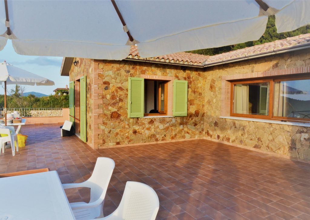 A stone building with green shutters, a tiled patio, and outdoor furniture.