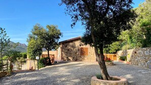 A stone building with a gravel driveway and a tree in a circular planter. - Villetta Zuccale (Capoliveri)