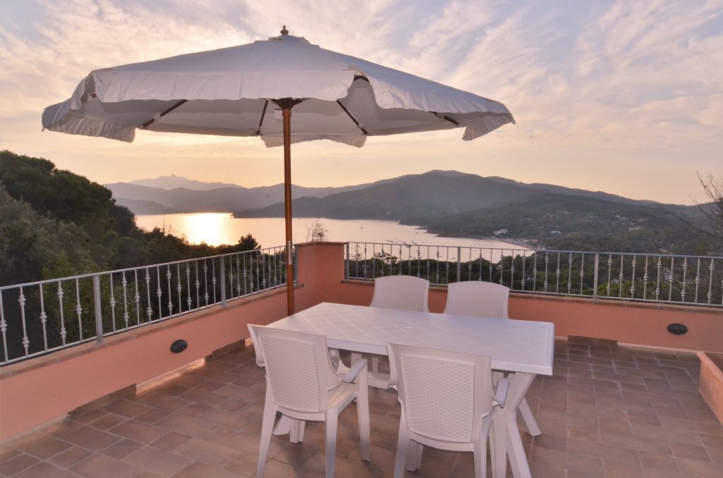 A terrace with a table and chairs, an umbrella, and a scenic view of mountains and a lake.