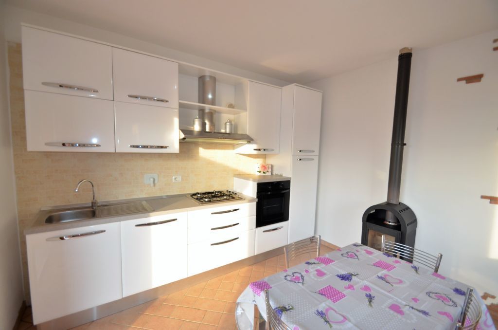 A compact kitchen with white cabinets, a gas stove, a black oven, and a wood-burning stove.