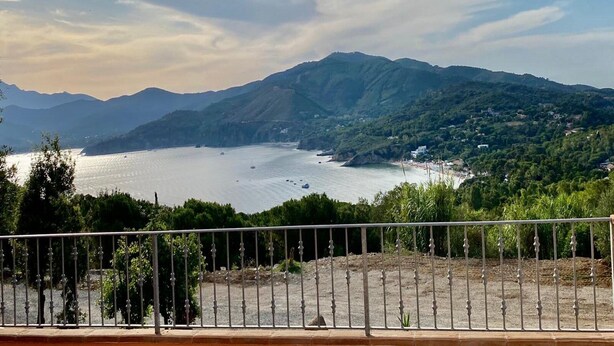 A coastal landscape with mountains in the background, a body of water, and a fenced area in the foreground. - Villetta Zuccale (Capoliveri)