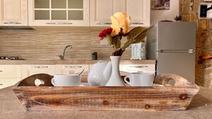 A kitchen with wooden cabinets, a white countertop, and a rustic wooden tray holding a vase with flowers and white cups. - Villetta Zuccale (Capoliveri)