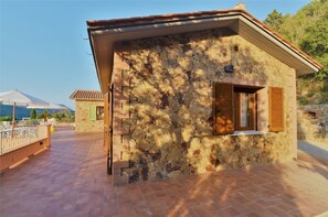 A stone building with a tiled patio, wooden shutters, and a view of the landscape.