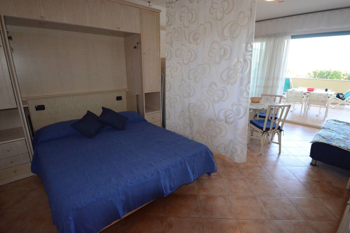 A bedroom with a large bed, a desk with a chair, and a balcony with a table and chairs.