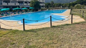 A swimming pool with lounge chairs and umbrellas, surrounded by a stone deck and a grassy area. - VerdeBlu (Capoliveri)