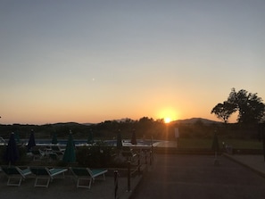 A sunset view with lounge chairs and umbrellas, a pool, and a distant mountain range. - VerdeBlu (Capoliveri)