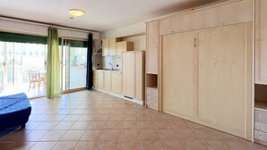 A spacious room with a kitchenette, a large wardrobe, and a sliding glass door leading to a balcony. - VerdeBlu (Capoliveri)