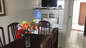 Una mesa de comedor con un florero, sillas de madera, un televisor sobre la barra y un dispensador de agua.