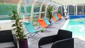 An indoor swimming pool with clear glass walls, surrounded by lounge chairs and potted plants. - Chemin des Dames Le Relais De Fleurette (Pontavert)