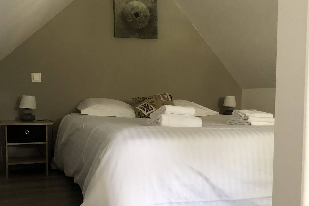 Ein Schlafzimmer mit geneigter Decke, einem Einzelbett mit weißer Bettwäsche, zwei Nachttischen mit Lampen und einem Wandbild.