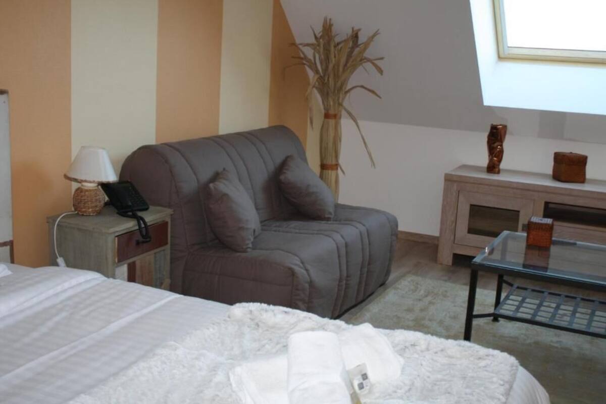 Ein Hotelzimmer mit einem Bett, einem grauen Sofa, einem kleinen Tisch, einer Lampe, einer Vase mit Trockenpflanzen und einem Fenster mit Blick.