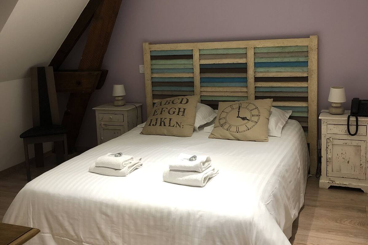 Ein Schlafzimmer mit schrägem Dach, einem Bett mit weißen Leinentüchern, zwei Nachttischen mit Lampen und einem Holzkopfende.