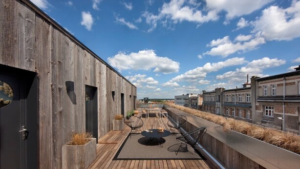 A rooftop terrace with a wooden deck, a round table with chairs, and a view of the cityscape.