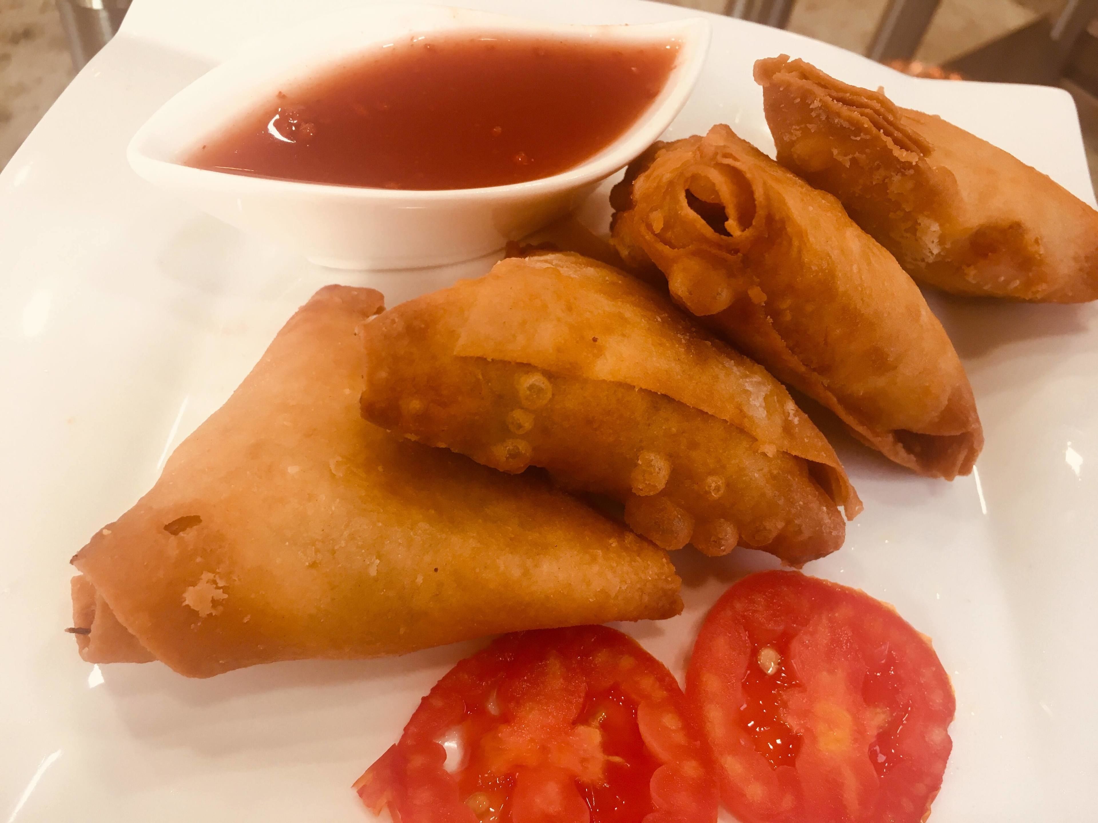 A plate of fried samosas with a side of tomato slices and a bowl of dipping sauce.