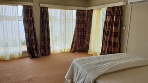 A hotel room with a bed, large windows with patterned curtains, and a carpeted floor. - Riverside Resort Villas (Bushrod Island)
