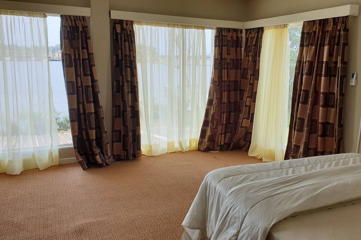 Habitació d'hotel amb llit, finestres grans amb cortines estampades i terra amb moqueta.