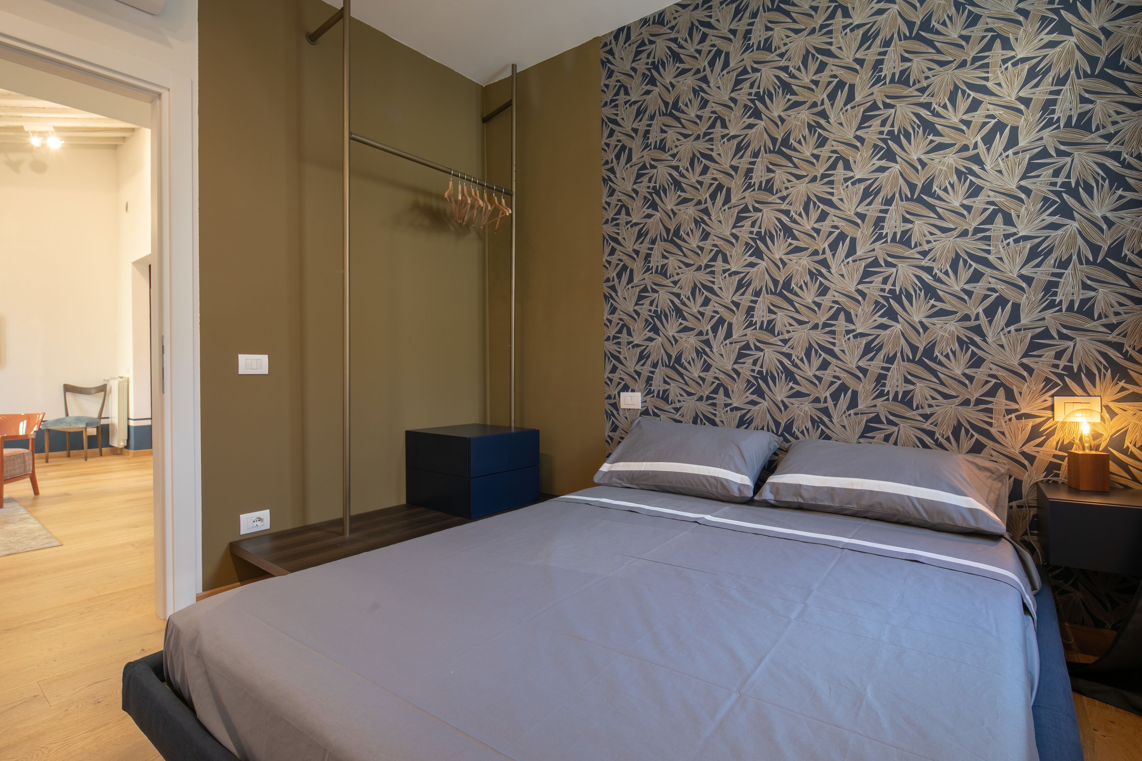Une chambre à coucher avec un lit, une table de chevet, une commode et un mur décoré d’un motif.