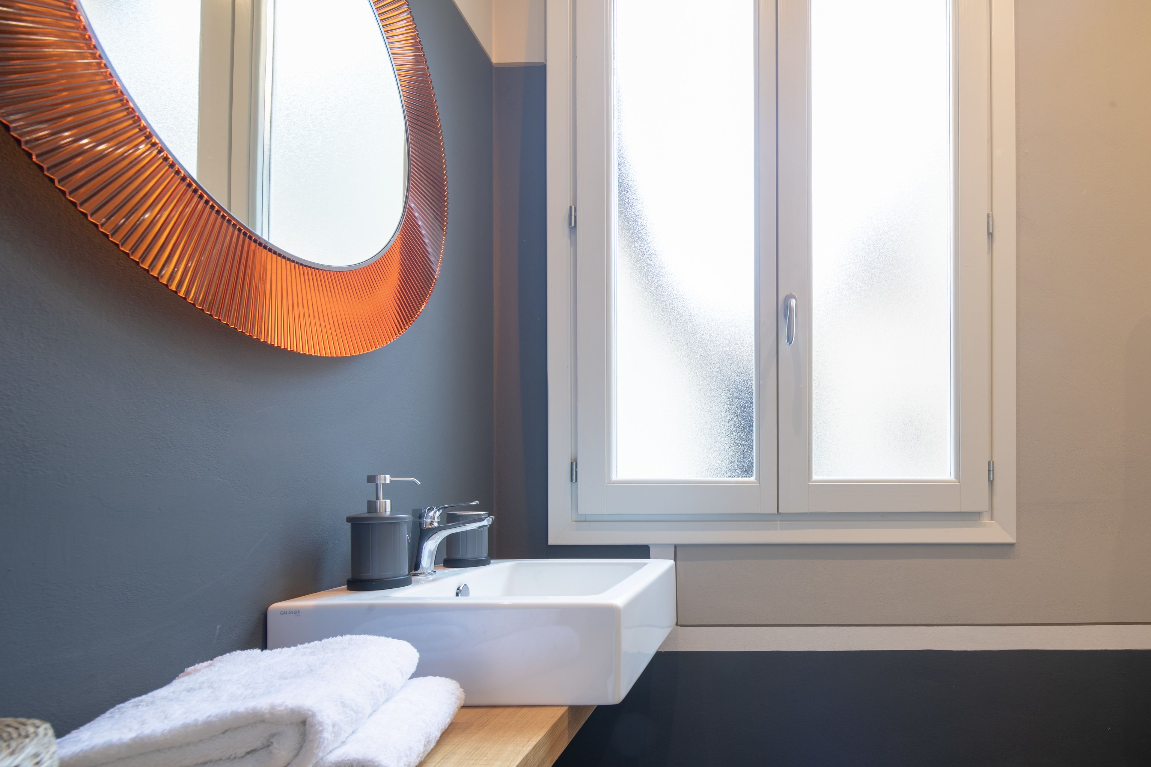 A modern bathroom with a large mirror, a white sink, and a window.
