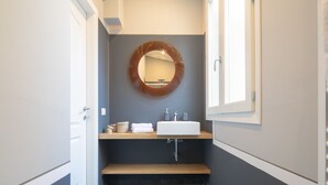 Ein modernes Badezimmer mit einem runden Spiegel, einem weißen Waschbecken und einer Holzbank.