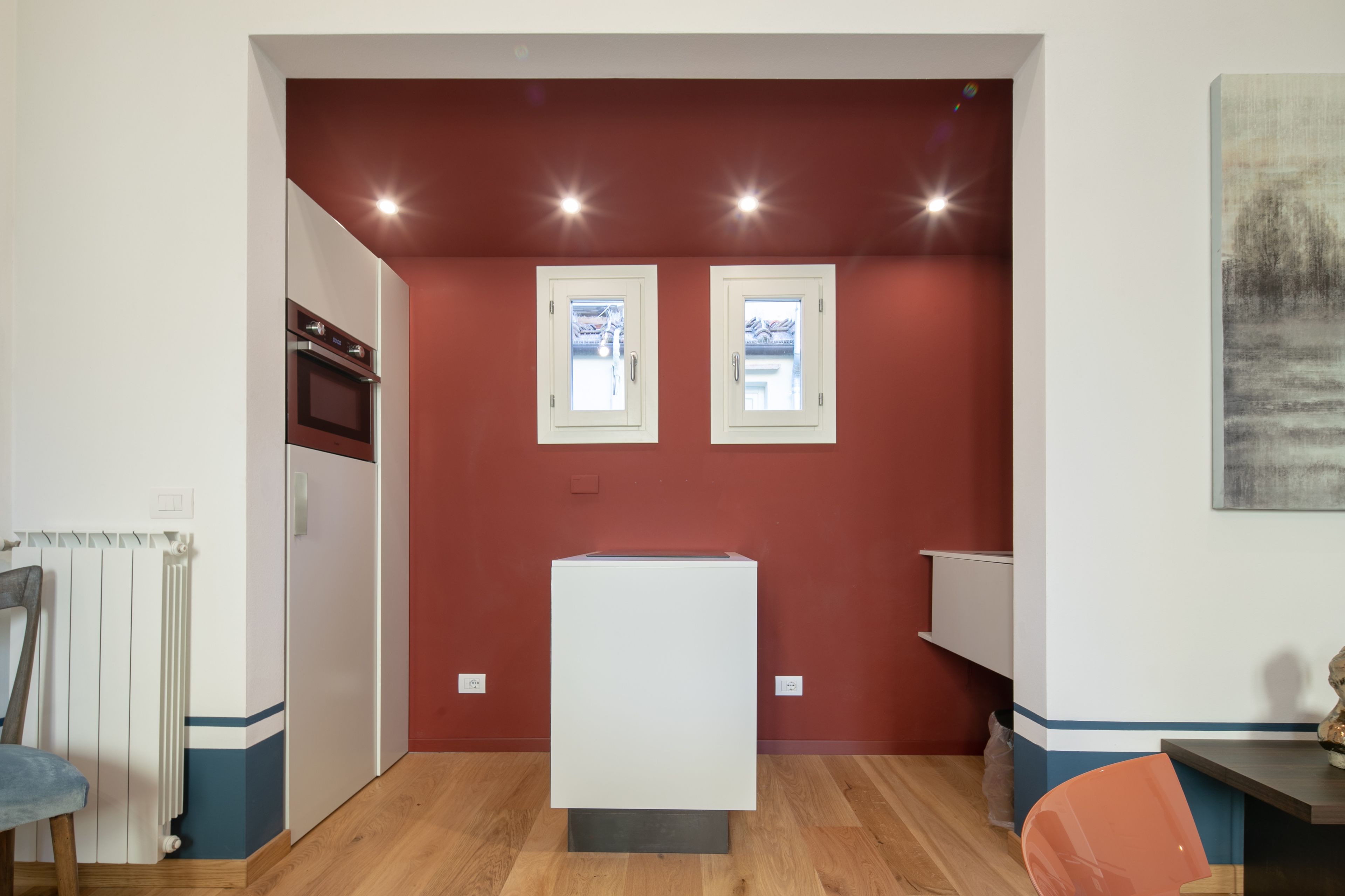 Une pièce de taille modeste, avec un réfrigérateur blanc, une chaise en bois, une petite table et un mur d’accent rouge.