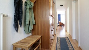 Un pasillo con un banco de madera, un perchero con abrigos y una alfombra estampada.