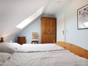 A bedroom with a sloped ceiling, a wooden wardrobe, a chair, and a bed.