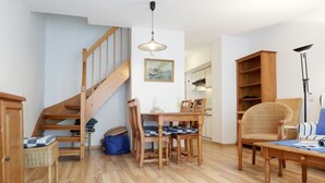 Un amplio salón con una escalera de madera, una zona de comedor con mobiliario de madera y una gran estantería.