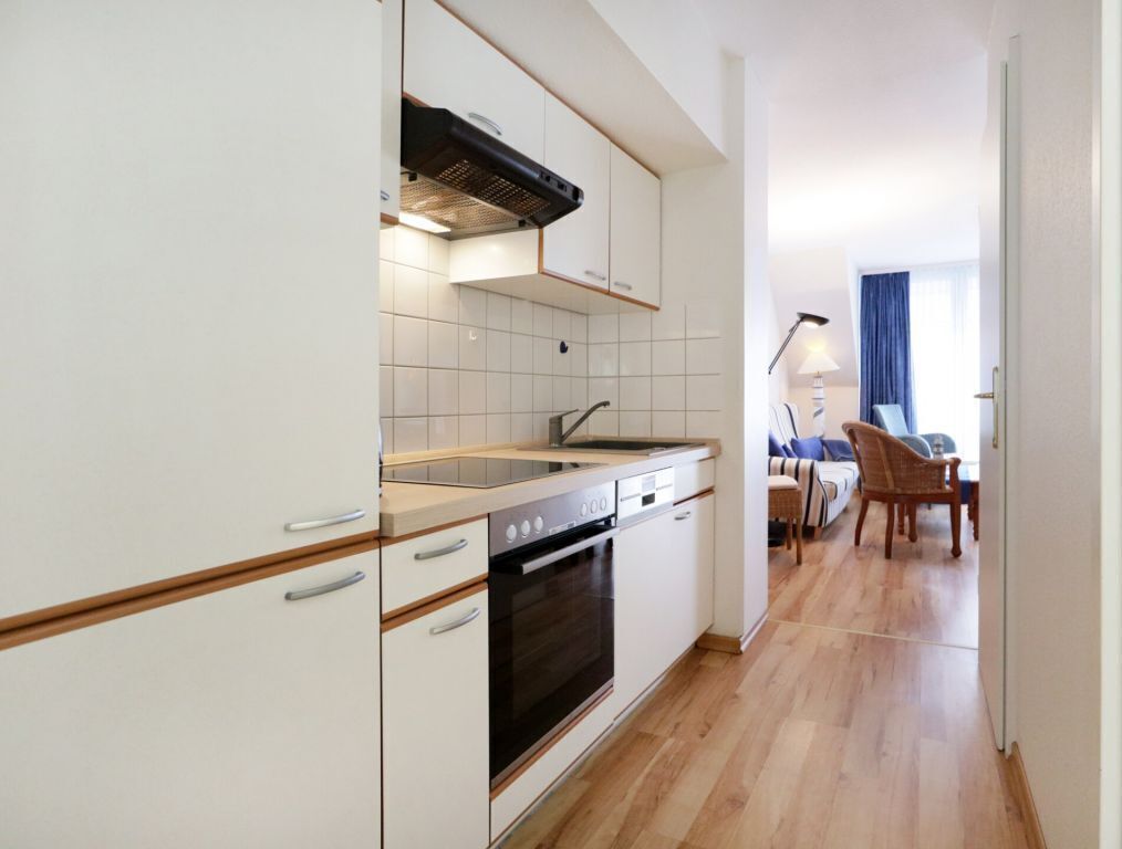 Une cuisine moderne avec des meubles blancs, un four encastré et un coin repas comprenant une table et des chaises.