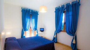 A hotel room with a bed, a desk with a computer, and blue curtains. - Luisa (Capoliveri)