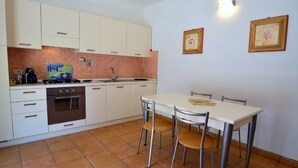 A compact kitchen with white cabinets, a stove, and a sink. There is a dining table with four chairs. - Luisa (Capoliveri)