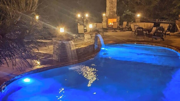 Una piscina con cascada, arquitectura de piedra y zona de estar al aire libre.