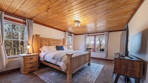 Un dormitorio con techo de madera, cama, mesita de noche, cómoda y ventana con cortinas.