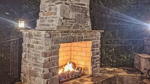 Chimenea de piedra al aire libre con fuego encendido, rodeada por un muro de piedra y una cerca de metal.