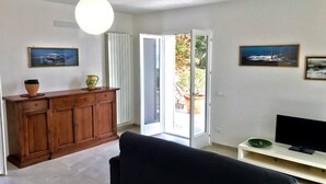 Uma sala de estar com um sofá escuro, um armário de madeira e uma televisão em um suporte.