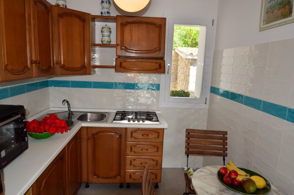 Cocina compacta con armarios de madera, estufa a gas, lavabo y ventana con vistas al verdor.