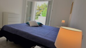 Quarto com cama, mesa de cabeceira com abajur e vista para o verde lá fora.