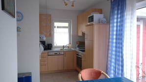 Cocina compacta con armarios de madera, microondas, lavamanos y comedor con mesa y silla.