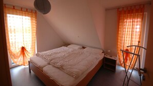 Un dormitorio con cama, mesita de noche, lámpara y ventana con cortinas.
