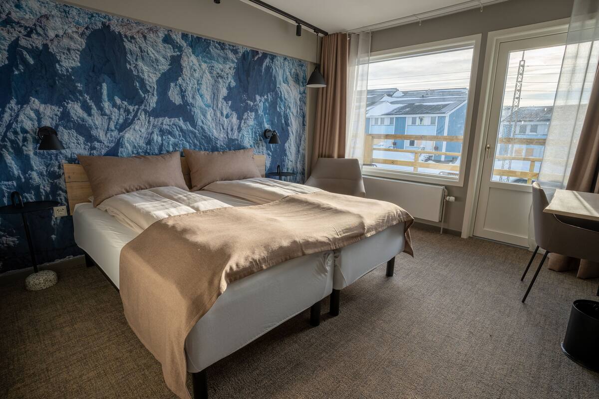 Een hotelkamer met een groot bed, een bureau, een stoel en uitzicht op gebouwen.