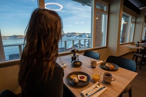 Un comedor con una mesa dispuesta para el desayuno, vistas al agua y un paisaje urbano de fondo.