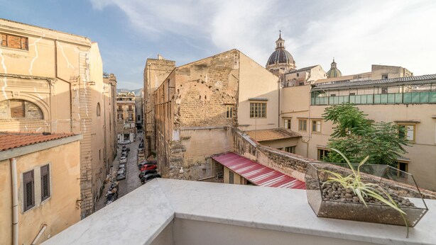 Una stretta via fiancheggiata da edifici, con un tendone rosso e cielo sereno.