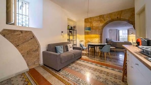 Un soggiorno moderno con un divano grigio, una zona pranzo con tavolo e sedie, e un angolo cottura con un bancone e un lavello.