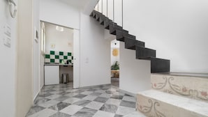 Un interno moderno con pavimento a scacchi, una scala con gradini neri e una zona cucina visibile attraverso un'apertura.