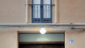 Un'imponente porta doppia in legno scuro con un cancello in metallo, un lampadario sopra e una piccola insegna appesa al muro sulla destra.